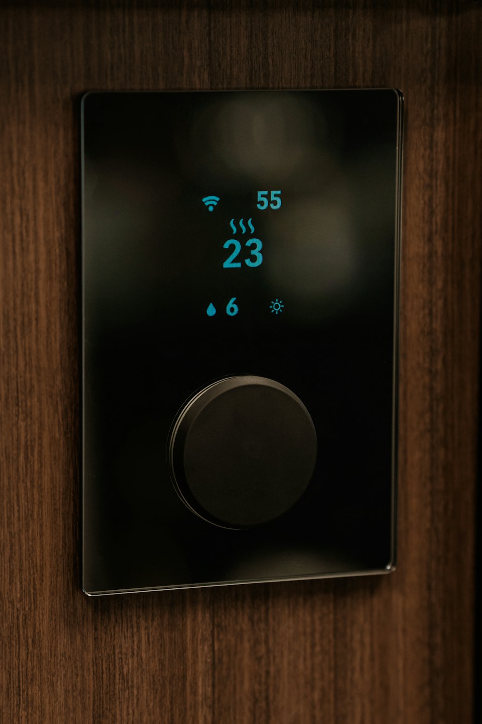 Smart thermostat with digital display mounted on wooden wall.